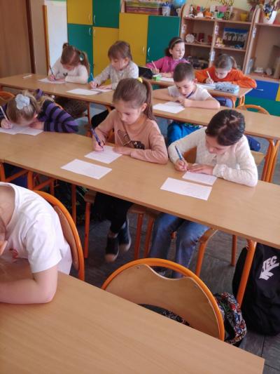 Dzieci biorące udział w szkolnym konkursie kaligrafii przepisują tekst wiersza na kartkę