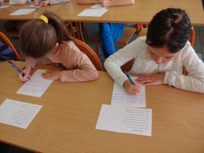 Dzieci biorące udział w szkolnym konkursie kaligrafii przepisują tekst wiersza na kartkę