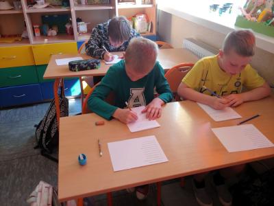 Dzieci biorące udział w szkolnym konkursie kaligrafii przepisują tekst wiersza na kartkę