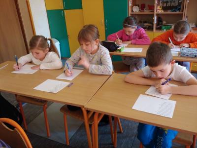 Dzieci biorące udział w szkolnym konkursie kaligrafii przepisują tekst wiersza na kartkę