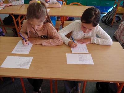 Dzieci biorące udział w szkolnym konkursie kaligrafii przepisują tekst wiersza na kartkę