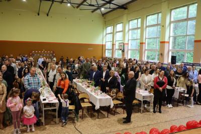 Zaproszeni goście stoją przy stołach i śpiewają sto lat
