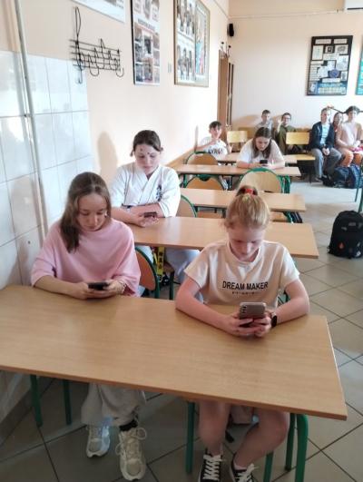 Na pierwszym planie uczennice rozwiązujące test przy użyciu telefonów.