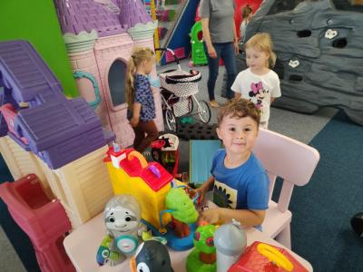 Chłopiec i dwie dziewczynki bawią się przy stoilku i dużym domku dla lalek.