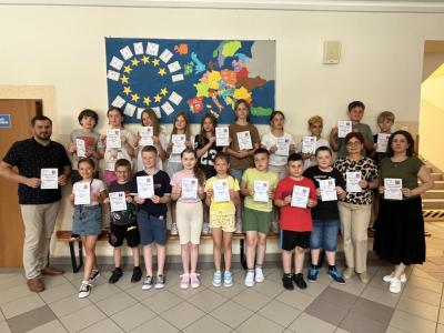 klasa 3a wraz z 3 nauczycielami stoi na szkolnym korytarzu z dyplomami za udział w projekcie