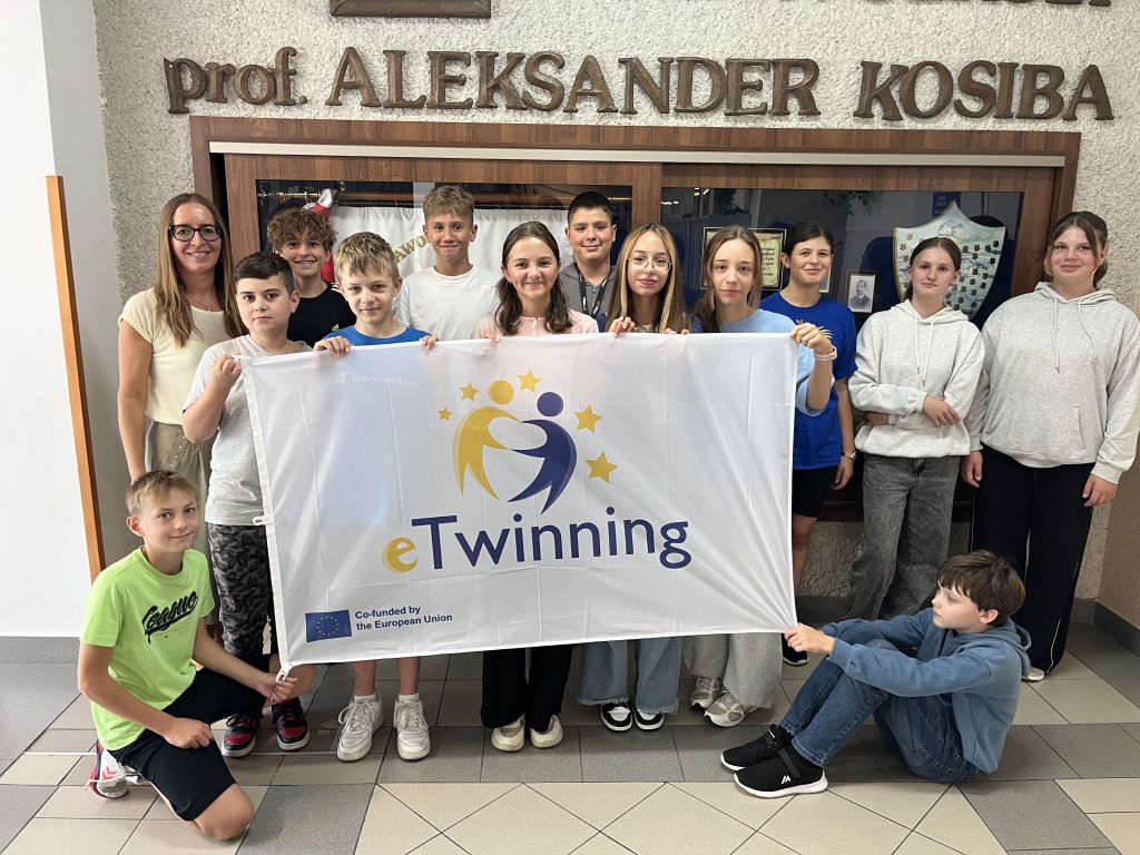 klasa 6b trzyma flagę z logo eTwinning na szkolnym korytarzu