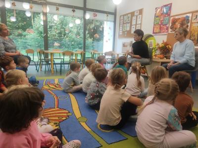 Pani Jola pokazuje ilustracje do opowiadania. Przed nią siedzą dzieci na dywanie.