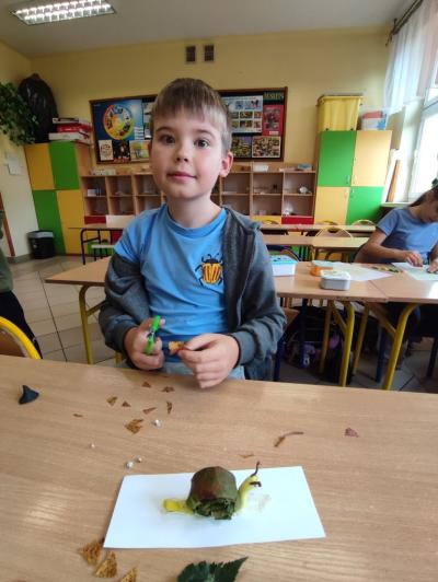 Uczeń prezentuje pracę plastyvznę wykonaną z plasteliny i liści.