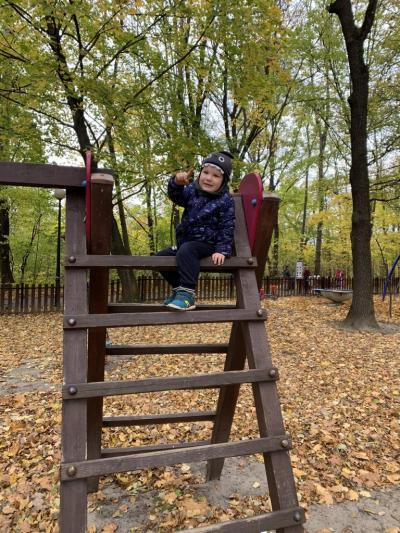 Chłopiec  siedzi na ostatnim szczebelku drabinki na placu zabaw w parku.