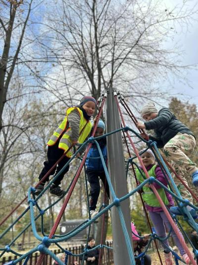 Czworo dzieci wspinają się po linach. W tle inne dzieci oraz korony drzew