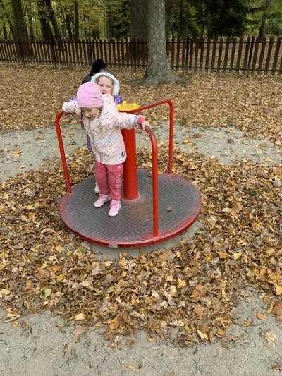 Dwie dziewczynki kręcą się na mini karuzeli na placu zabaw  w parku