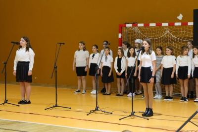 Na pierwszym planie dwie dziewczynki recytujące wiersz, w tle chór