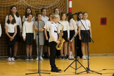 Uczeń klasy 5 grający na saksofonie - w tle chór szkolny.