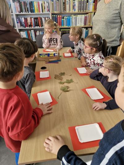 Dzieci stoją przy stoliku i odbijają jesienne liście w glinie