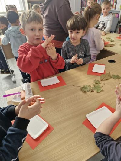 Dzieci stoją przy stoliku i odbijają jesienne liście w glinie