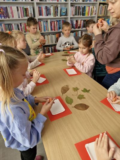 Dzieci stoją przy stoliku i odbijają jesienne liście w glinie