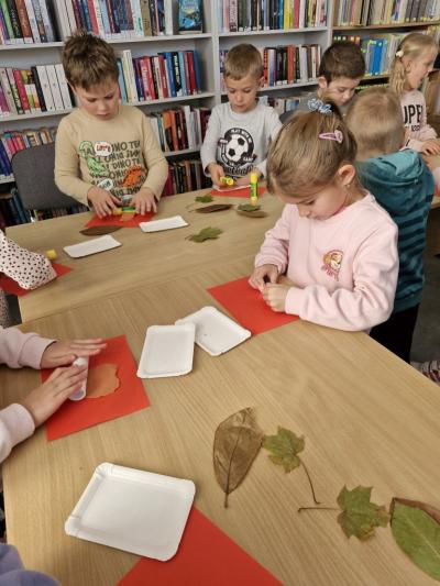 Dzieci stoją przy stoliku i odbijają jesienne liście w glinie