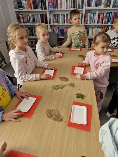 Dzieci stoją przy stoliku i odbijają jesienne liście w glinie