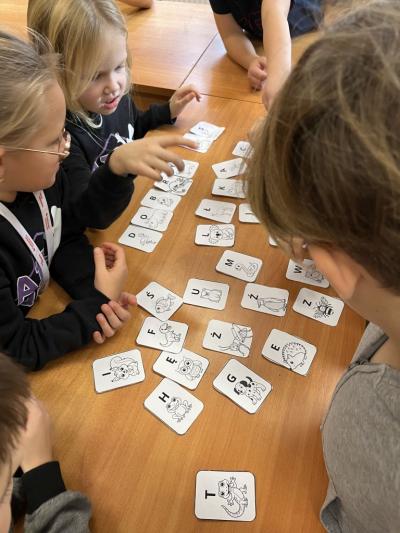 grupa kilku dzieci na świetlicy szkolnej układa na ławce zaszyfrowaną wiadmosć z alfabetu zwierzęcego.