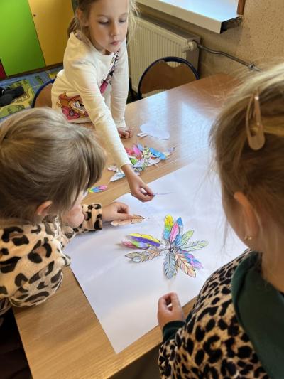 trzy dziewczynki projketują skrzydła ptaka z kolorowych papierowych piórek.