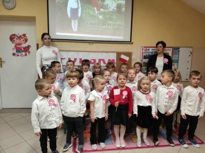 Dzieci z grupy Biedronki, ubrane galowo, wraz z paniami podczas śpiewu hymnu Polski z okazji Święta Niepodległości.