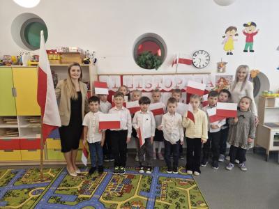 Dzieci z wychowawcami stoją z flagami Polski i śpiewają hymn narodowy