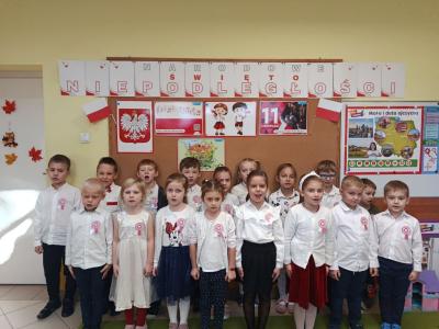 Grupa Skrzaty ubrana w odświętne stroje z kotylionami na piersi z dumą śpiewa hymn.