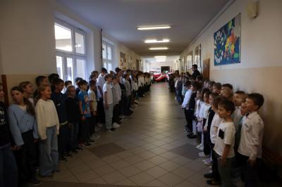 Uczniowie podczas apelu odśpiewują hymn polski. W tle flagi Polski.