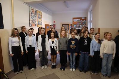 Uczniowie podczas apelu odśpiewują hymn polski. W tle flagi Polski.