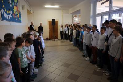 Uczniowie podczas apelu odśpiewują hymn polski. W tle flagi Polski.
