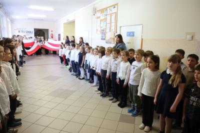 Uczniowie podczas apelu odśpiewują hymn polski. W tle flagi Polski.