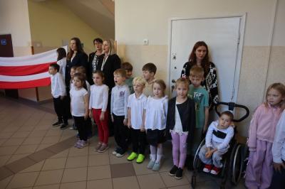 Uczniowie podczas apelu odśpiewują hymn polski. W tle flagi Polski.