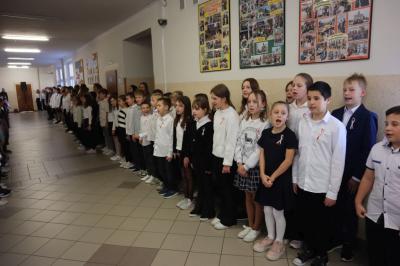 Uczniowie podczas apelu odśpiewują hymn polski. W tle flagi Polski.