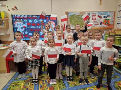 Uczniowie podczas apelu odśpiewują hymn polski. W tle flagi Polski.