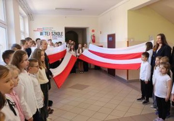 Uczniowie podczas apelu odśpiewują hymn polski. W tle flagi Polski.