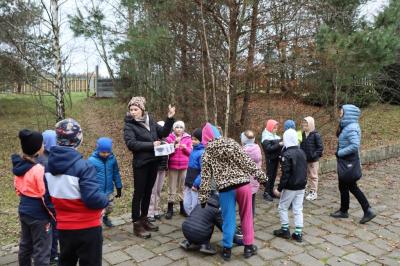 Dzieci idą ścieżką edukacyjną, słuchają co mówi pani przewodnik.