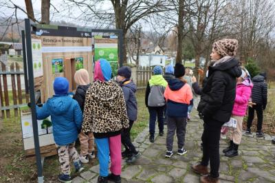 Dzieci idą ścieżką edukacyjną, słuchają co mówi pani przewodnik