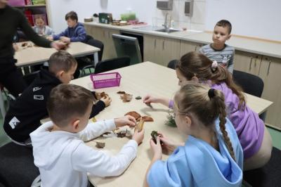 Dzieci siedzą przy stoliku podczas warsztatówrozpoznawania drzew po liściach..