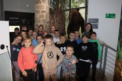Grupka uczniów pozuje z wychowawcą do zdjęcia w muzeum przyrodniczym, w tle niedźwiedź.