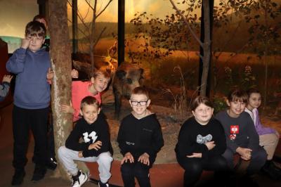 Uczniowie pozują do zdjęcia, za nimi ekspozycja zwierząt leśnych.