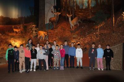 Uczniowie pozują do zdjęcia, za nimi ekspozycja zwierząt leśnych.