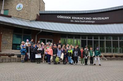 Uczniowie z dwoma paniami stoją na schodach przed budynkiem