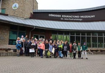 Uczniowie z dwoma paniami stoją na schodach przed budynkiem.