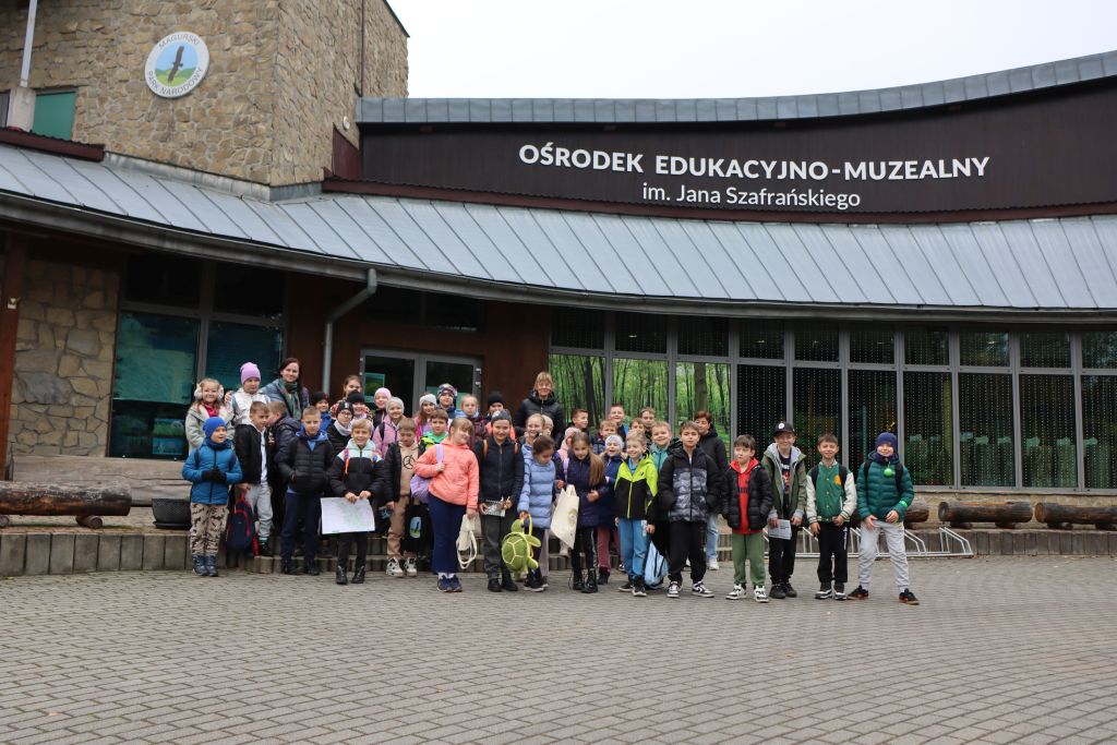 Uczniowie z dwoma paniami stoją na schodach przed budynkiem.