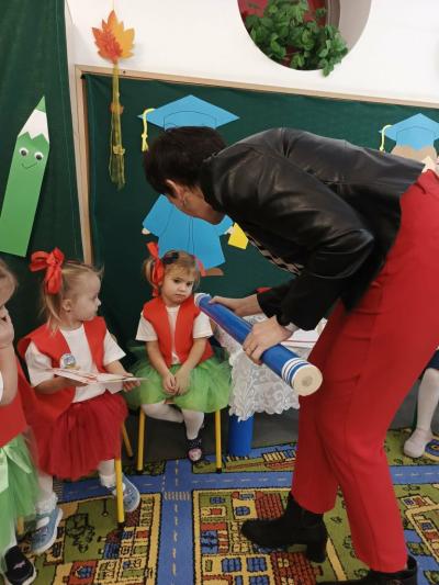 Pani dyrektor pasuje diewczynkę na przedszkolaka ołówkiem