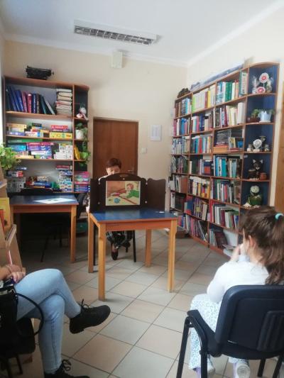 Na zdjęciu bibliotekarka czyta uczniom opowiadanie w teatrzyku kamishibai..