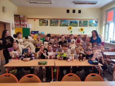 Uczniowie pozuja do zdjęcia, trzymająć przyniesione przez siebie pluszowe misie.