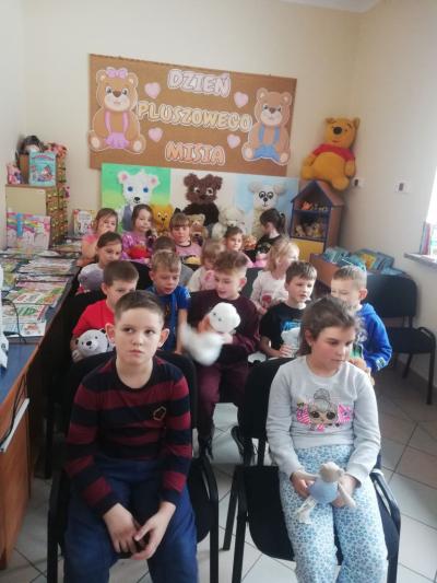 Uczniowie siedzą w czytelni i słuchają historii Dnia Pluszowego Misia.