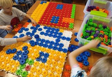 Uczniowie układają domek z różnych figur geometrycznych.