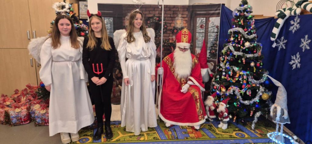 Święty Mikołaj z dwoma aniołkami i diabełkiem pozują do zdjęcia.